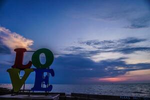 avvicinamento Visualizza di il parola amore posto su il costa contro un' tramonto cielo con vuoto spazio per fotocopiatura. foto