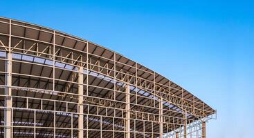 parte di grande metallo industriale fabbrica edificio struttura con ondulato acciaio curva tetto e lucernari nel costruzione luogo contro blu cielo sfondo, Basso angolo Visualizza con copia spazio foto