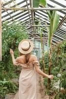 un' bellissimo giovane donna prende cura di impianti nel un' serra. il Visualizza a partire dal il Indietro. concetto di giardinaggio e un eco-friendly stile di vita. foto