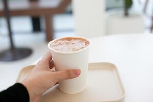 caldo cacao cioccolato nel carta tazza Tenere di umano mano con bianca caldo tono bar sfondo foto