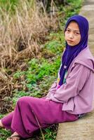 lato Visualizza di un' donna indossare un' foulard seduta accanto un' riso campo strada nel il mattina. foto