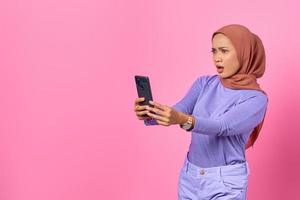 scioccata giovane donna asiatica guardando lo schermo del telefono cellulare su sfondo rosa