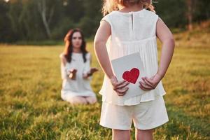 la figlia del bambino si congratula con sua madre e le regala una cartolina. madre e ragazza sorridono e si abbracciano. foto