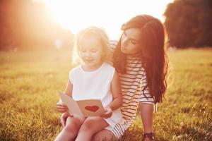 la figlia del bambino si congratula con sua madre e le regala una cartolina. madre e ragazza sorridono e si abbracciano. foto