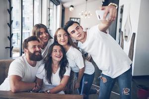 un gruppo di persone fa una foto selfie in un bar. i migliori amici si sono riuniti a tavola mangiando pizza e cantando vari drink
