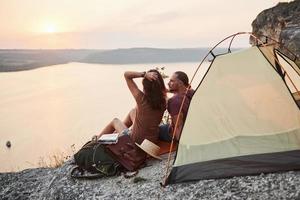 foto di una coppia felice seduta in tenda con vista sul lago durante un'escursione. concetto di vacanze avventura stile di vita di viaggio