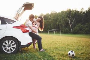 la coppia sposata abbastanza giovane e la loro figlia stanno riposando nella natura. la madre, il padre e la bambina sono seduti sul bagagliaio della macchina aperto foto