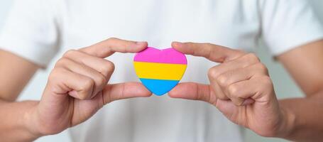 pansexual orgoglio giorno e lgbt orgoglio mese concetto. mano Tenere rosa, giallo e blu cuore forma per lesbica, gay, bisessuale, transgender, strano e pansexual Comunità foto