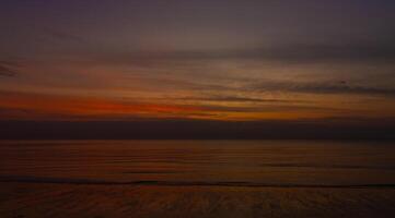 sagome un' sereno tramonto al di sopra di il spiaggia, il cielo di arancia e getto foto