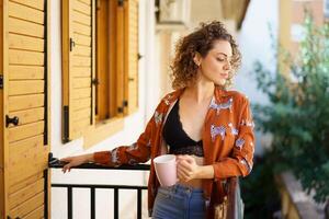 giovane donna in piedi su balcone con tazza di caffè foto