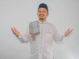 musulmano asiatico uomo sorridente a il telecamera con braccia Aperto fare accogliente gesto foto