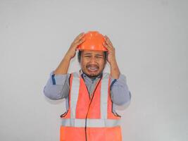 impaurito asiatico uomo costruttore lavoratore uomo è Tenere il suo mani su il suo testa con largo Aperto bocca isolato su bianca sfondo. foto