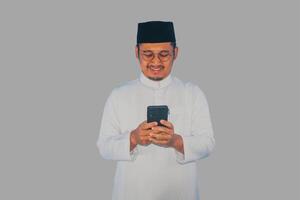 musulmano asiatico uomo sorridente contento quando sms utilizzando il suo mobile Telefono foto
