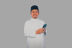 musulmano asiatico uomo sorridente a telecamera mentre Tenere il suo mobile Telefono foto