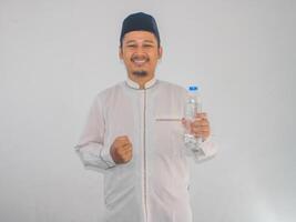 musulmano asiatico uomo sorridente a il telecamera mentre Tenere un' bottiglia di potabile acqua foto