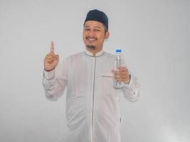 musulmano asiatico uomo sorridente e puntamento dito su mentre Tenere un' bottiglia di potabile acqua foto