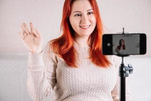 una giovane blogger dai capelli rossi conduce un flusso online utilizzando lo smartphone. foto