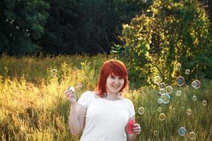 sorridente giovane donna dai capelli rossi con bolle di sapone. foto