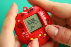 kiev, Ucraina - marzo 9, 2024 retrò animale domestico portachiavi gioco tamagotchi nel rosso plastica Astuccio nel femmina mani foto