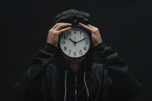 giovane uomo Tenere grande orologio copertura il suo viso al di sopra di nero sfondo foto