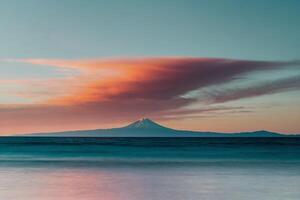 un' tramonto al di sopra di il acqua con montagne nel il sfondo foto