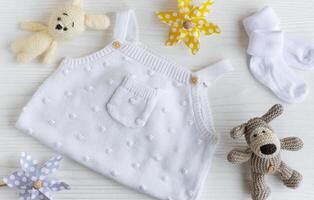 impostato di bianca Abiti e Accessori per neonato bambino. a maglia giocattoli, a maglia pagliaccetto, calzini su bianca di legno sfondo. foto
