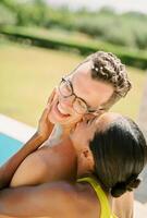 sorridente donna baci uomo su il guancia mentre abbracciare il suo viso a partire dal dietro. indietro Visualizza foto