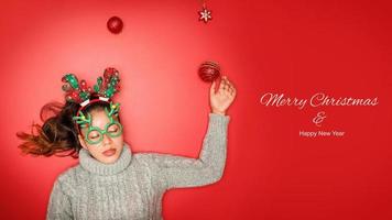 natale capodanno. giovane donna vestita in maglione caldo con oggetti di scena palla rossa con ornamenti natalizi in vacanza su sfondo rosso brillante. concetto buon natale. foto