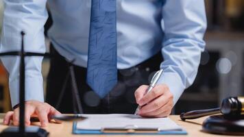 un' avvocato nel un' blu camicia e nero pantaloni è scrittura e firma su un' pezzo di carta documento con un' penna su il ufficio foto