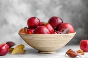 belle mele rosse fresche con foglie autunnali in un vaso di legno foto