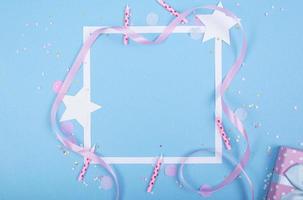 sfondo vacanza festa con nastro, stelle, candele di compleanno, scatola regalo cornice vuota e coriandoli su sfondo blu foto