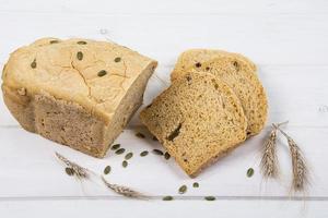 pane rustico con lievito di grano con semi di zucca su fondo di legno bianco foto