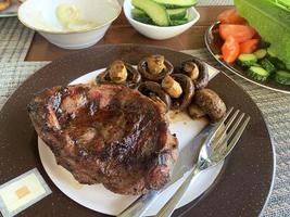 bistecca di agnello alla griglia, funghi prataioli, verdure in tavola foto