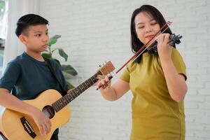 asiatico ragazzo giocando chitarra e madre giocando violino, sentire apprezzato e incoraggiato. concetto di un' contento famiglia, apprendimento e divertimento stile di vita, amore famiglia cravatte foto