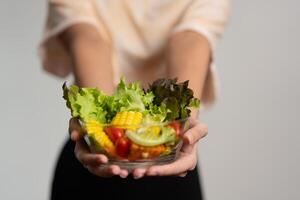 ritratto di un' contento giocoso asiatico ragazza mangiare fresco insalata a partire dal un' bicchiere ciotola dopo allenarsi a casa. giovane signora godendo salutare nutrizione e biologico cibo, avendo vegetariano pasto foto