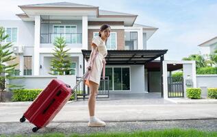 un' giovane asiatico donna con bagaglio in piedi nel davanti di un' nuovo acquisto casa per mossa in un' nuovo Casa. inizio vita a proprio o affittato piatto concetto e in movimento giorno concetto. foto