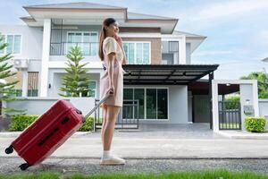 un' giovane asiatico donna con bagaglio in piedi nel davanti di un' nuovo acquisto casa per mossa in un' nuovo Casa. inizio vita a proprio o affittato piatto concetto e in movimento giorno concetto. foto