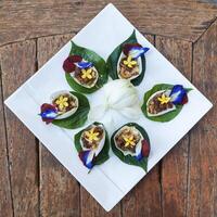 miang kham tailandese cibo consiste di cha Phlu foglie, arrostito noce di cocco, aglio, noccioline, Zenzero, avvolto nel bianca loto petali. foto