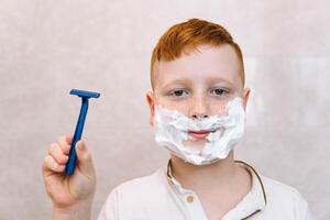 divertente ragazzo nel il bagno con rasatura crema su il suo viso e rasatura rasoio foto