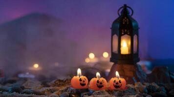 Halloween sfondo, 3 a forma di zucca candele nel il primo piano, un vecchio lampada su un' roccia contro un' blu sfocato sfondo foto