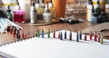piccolo colorato matite su bianca carta su un' di legno tavolo con arte forniture nel il sfondo foto