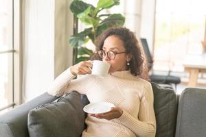 donna latina che beve caffè sul divano di casa foto