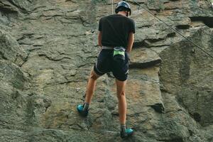 giovane uomo nel attrezzatura fare roccia arrampicata all'aperto. formazione la zona per all'aperto attività. estremo sport. foto