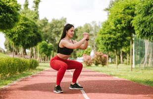 bellissimo donna fare fitness esercizio nel mattina all'aperto. fare squat nel un all'aperto parco foto