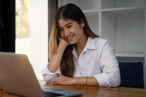 allegro giovane asiatico donna utilizzando il computer portatile computer a casa. alunno femmina nel vivente camera. in linea apprendimento, studiando , in linea acquisti, libero professionista, ASEAN concetto. foto