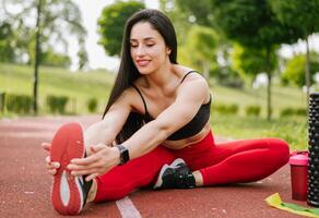 un' sorridente donna nel abbigliamento sportivo è riscaldamento su e allungamento prima formazione nel il parco. salutare stile di vita concetto foto