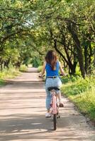 posteriore indietro Visualizza di un' giovane donna equitazione un' bicicletta nel un' città parco a estate. foto