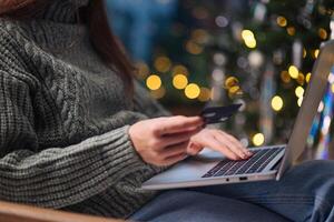 Natale in linea acquisti, i saldi e sconti promozioni durante inverno vacanze, in linea shopping a casa. femmina mani su il il computer portatile con credito carta e sfocato bokeh luci foto