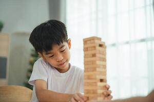 un' giovane ragazzo è giocando con un' di legno bloccare Torre. lui è focalizzata su il gioco e lui è godendo lui stesso foto