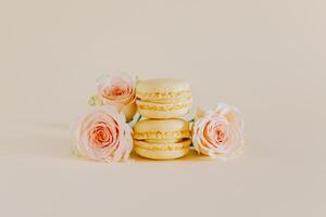 gustoso giallo francese macarons con tenero rosa fiori su un' pesca pastello sfondo. foto